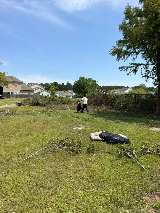 A lawn with cut brush and branches piled for removal and a person working near the fence line