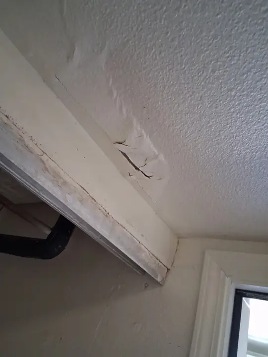 A cracked and bubbled section of textured ceiling drywall above a window