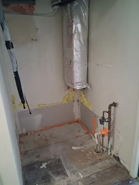 A closet with the lower drywall removed, orange supply lines along the floor and a copper stub with a valve