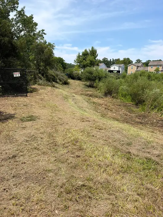 A long mowed strip of grass beside a chain-link fence with houses beyond