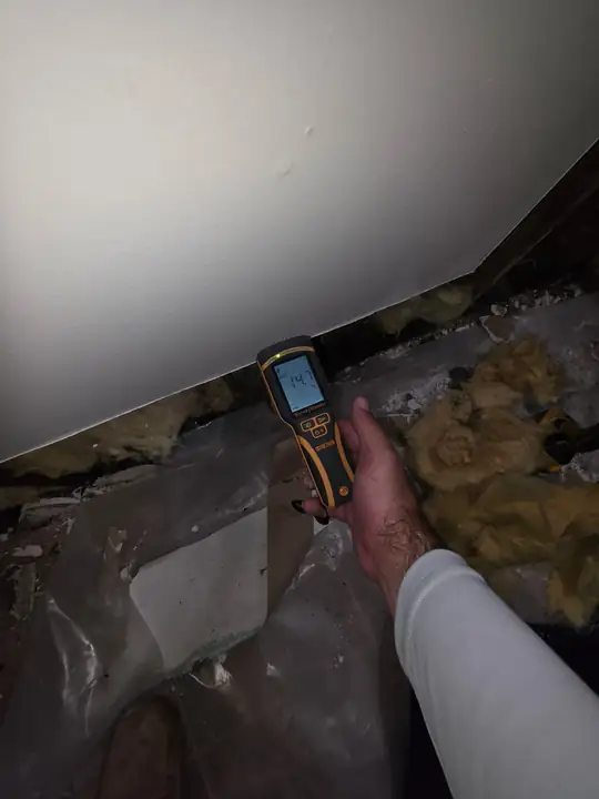 A hand holding a moisture meter against damp insulation in a tight space